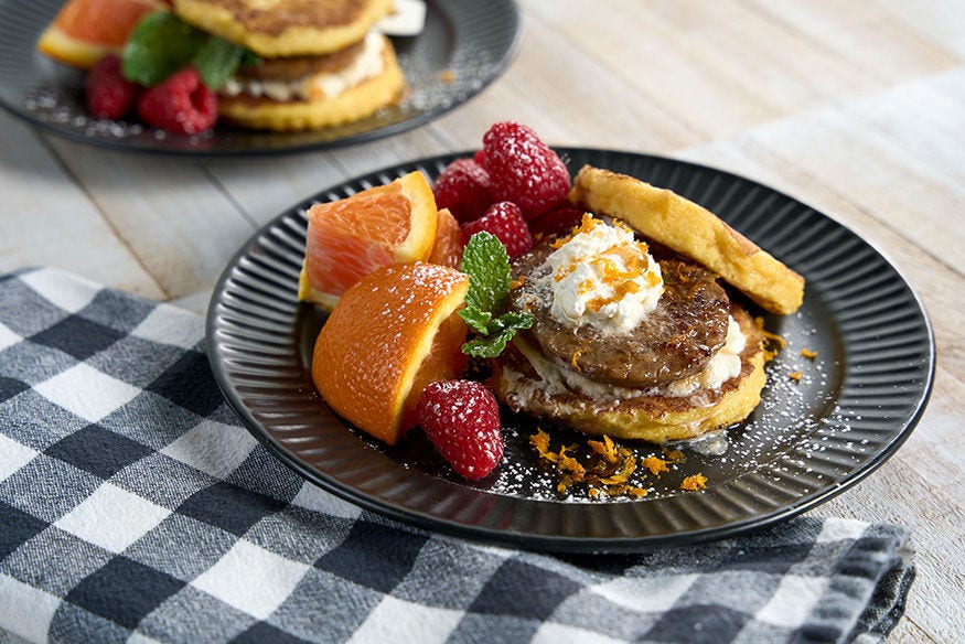 French toast topped with breakfast sausage with a side of sliced oranges and raspberries