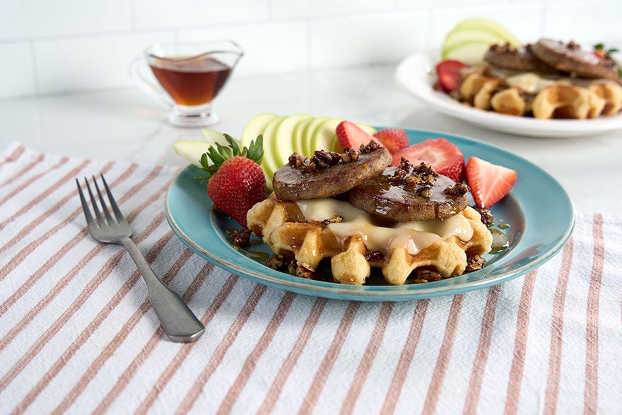 waffle topped with sausage with a side of strawberries